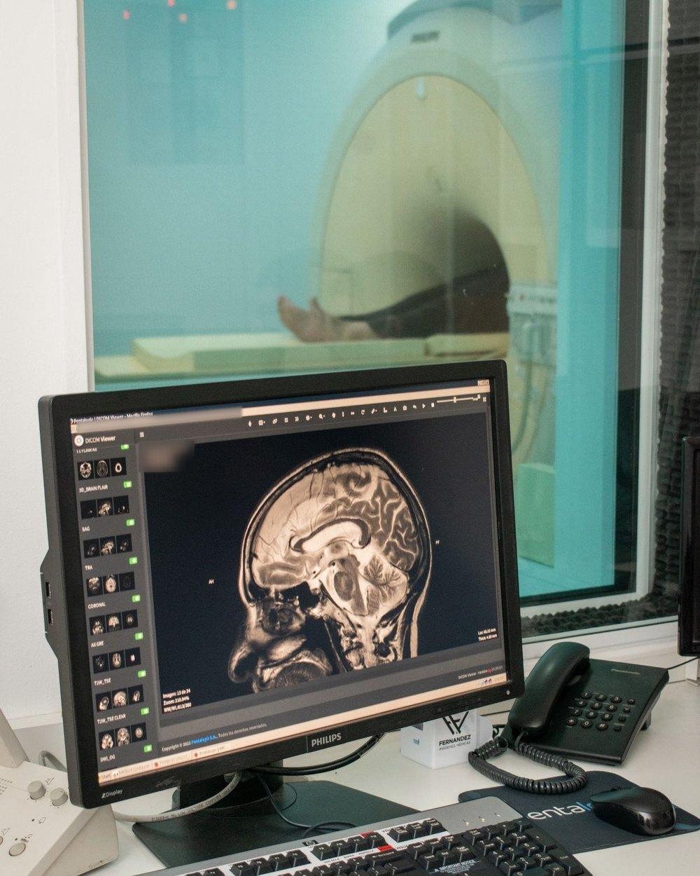 Consola de un resonador en un centro de salud cliente: el visor DICOM de Pentalogic muestra una resonancia de encéfalo y, detrás del vidrio, el equipo con el paciente. Los datos del paciente están difuminados.
